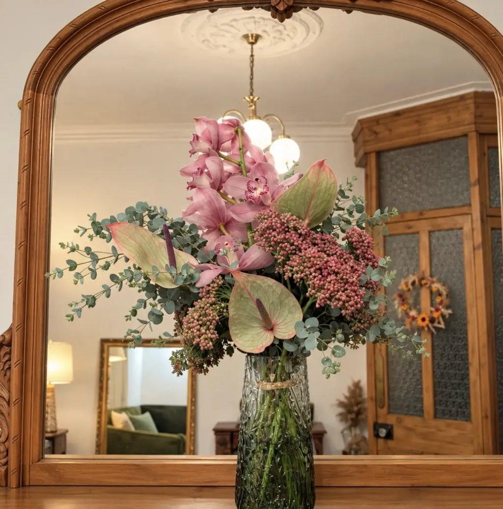 Pink orchid and anthurium arrangement in a green glass vase