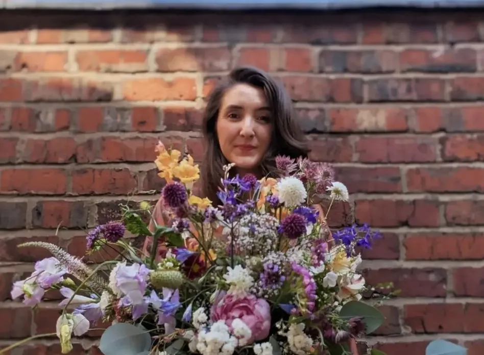 Sophia holding a wild, garden-style bouquet against a brick wall